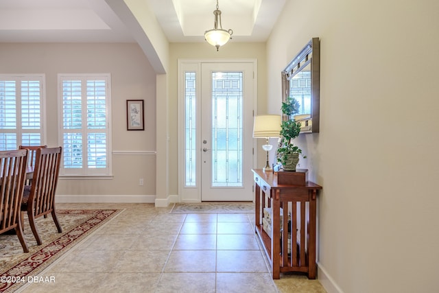 entryway with light tile patterned flooring, a healthy amount of sunlight, and a raised ceiling