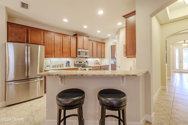 kitchen featuring light stone countertops, appliances with stainless steel finishes, backsplash, and a breakfast bar area