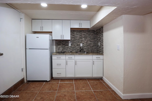 kitchen featuring white cabinets, stone counters, white fridge, and backsplash