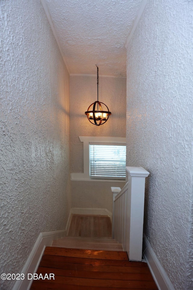 staircase with hardwood / wood-style flooring, a textured ceiling, and ornamental molding