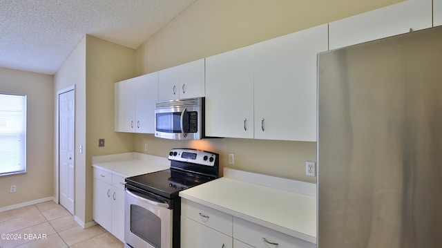 kitchen featuring lofted ceiling, white cabinets, a textured ceiling, light tile patterned floors, and appliances with stainless steel finishes