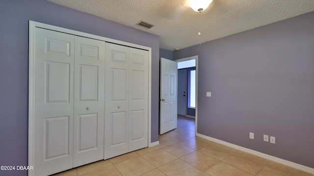 unfurnished bedroom featuring light tile patterned flooring, a textured ceiling, and a closet