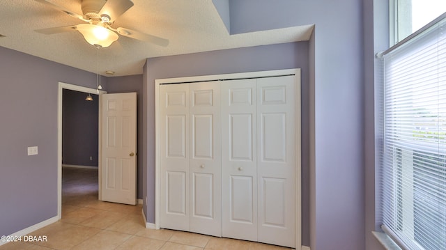 unfurnished bedroom featuring a closet, light tile patterned flooring, ceiling fan, and a textured ceiling