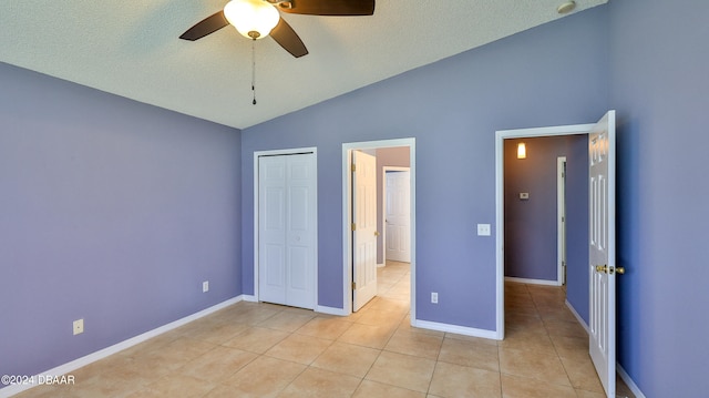 unfurnished bedroom featuring ceiling fan, a textured ceiling, light tile patterned floors, a closet, and vaulted ceiling