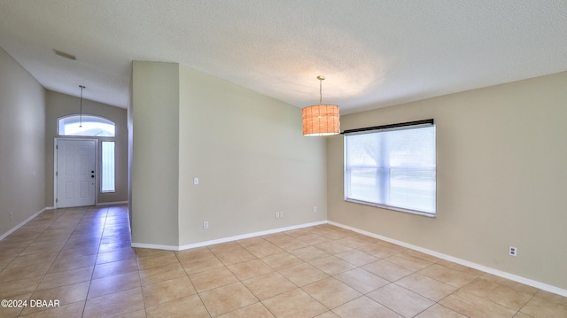 tiled empty room featuring a textured ceiling and vaulted ceiling