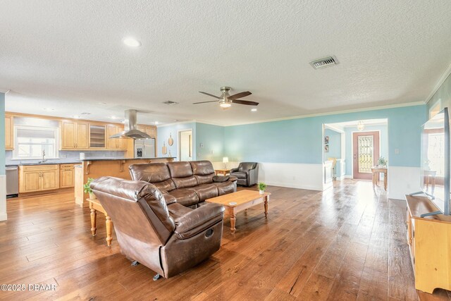 living area with light wood-style flooring, crown molding, visible vents, and plenty of natural light