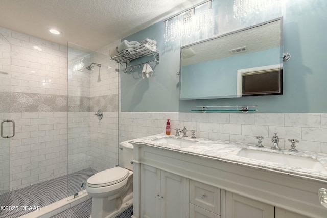 full bath with a sink, visible vents, a textured ceiling, and tile walls