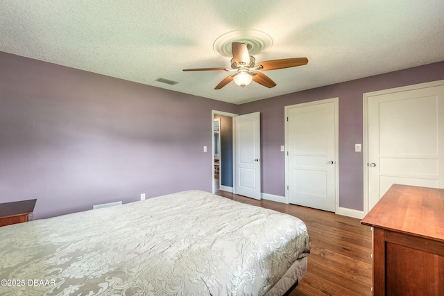 bedroom with dark wood-style floors, baseboards, visible vents, a textured ceiling, and ceiling fan