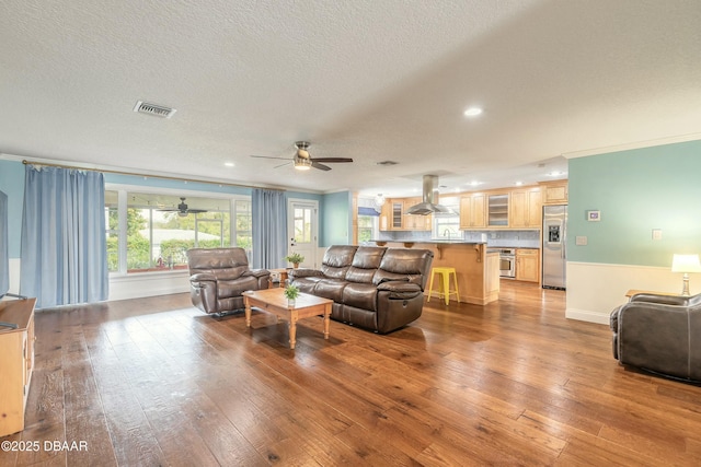 living room featuring ornamental molding, a textured ceiling, light wood finished floors, and visible vents