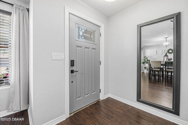 entrance foyer with dark wood-type flooring, a textured wall, and baseboards