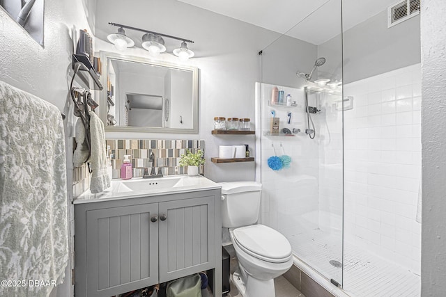 full bath featuring toilet, tiled shower, visible vents, decorative backsplash, and vanity