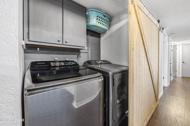 laundry room with a barn door, washing machine and clothes dryer, wood finished floors, a textured ceiling, and cabinet space