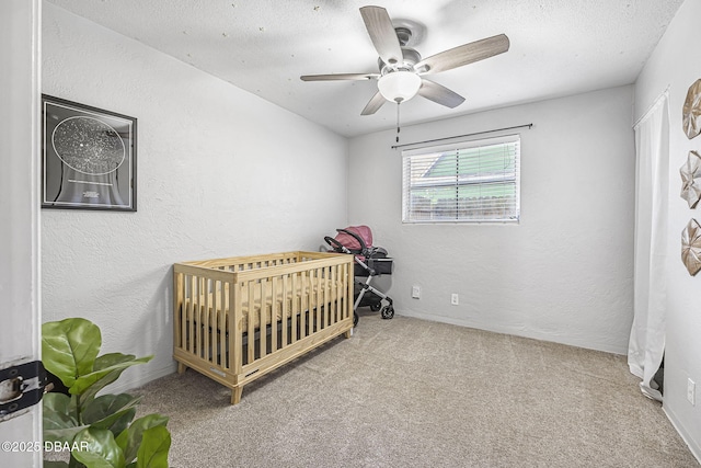 carpeted bedroom featuring a nursery area, a textured wall, and a ceiling fan