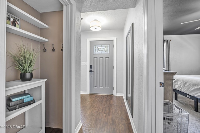 doorway to outside featuring a textured ceiling, a ceiling fan, baseboards, and dark wood-style flooring