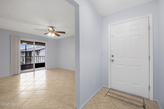 foyer entrance featuring a textured ceiling, baseboards, a ceiling fan, and light tile patterned flooring