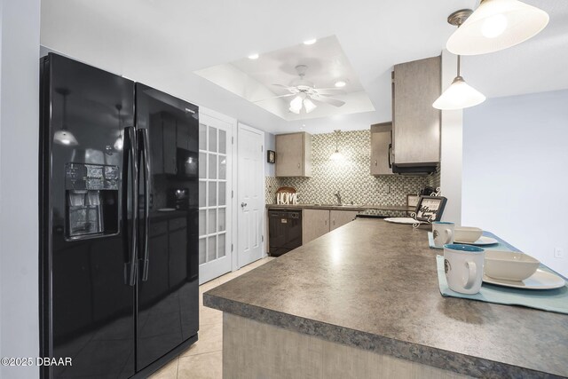 kitchen with dark countertops, black appliances, a tray ceiling, and backsplash