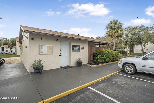 exterior space with uncovered parking, a shingled roof, and stucco siding