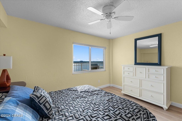 bedroom featuring a water view, ceiling fan, light hardwood / wood-style flooring, and a textured ceiling