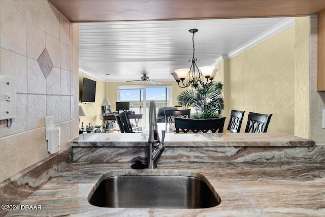 kitchen with pendant lighting, sink, crown molding, and ceiling fan with notable chandelier