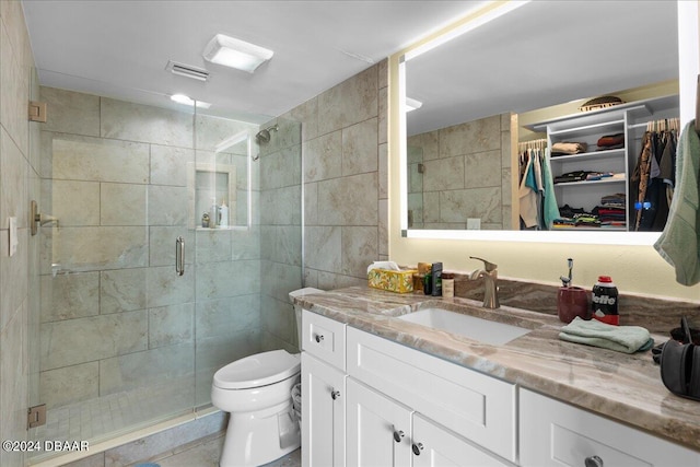 bathroom featuring tile walls, vanity, toilet, a shower with door, and tile patterned floors