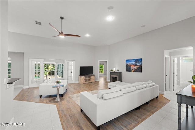 living room featuring light wood-type flooring, ceiling fan, and a high ceiling