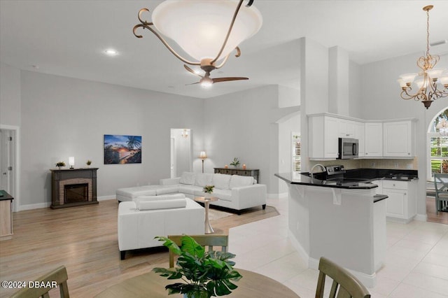 living room with ceiling fan with notable chandelier, light hardwood / wood-style floors, sink, and a high ceiling