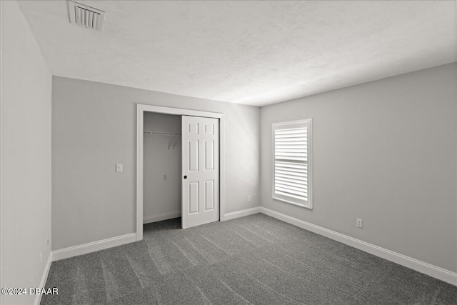 unfurnished bedroom featuring a textured ceiling, a closet, and dark carpet