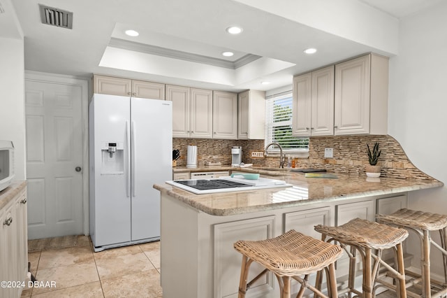 kitchen with kitchen peninsula, white appliances, a kitchen bar, and a raised ceiling