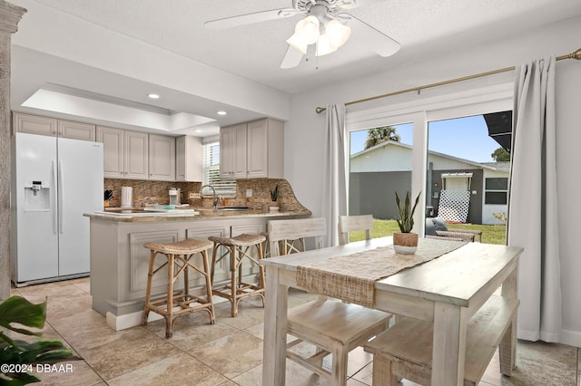 kitchen featuring backsplash, a textured ceiling, white fridge with ice dispenser, a kitchen breakfast bar, and kitchen peninsula