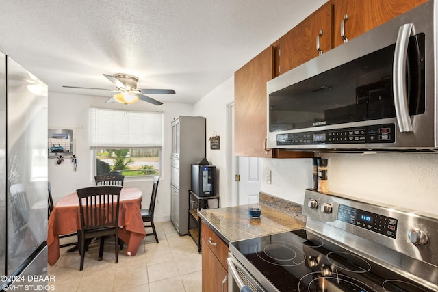 kitchen featuring stainless steel appliances, dark stone counters, a textured ceiling, light tile patterned floors, and ceiling fan