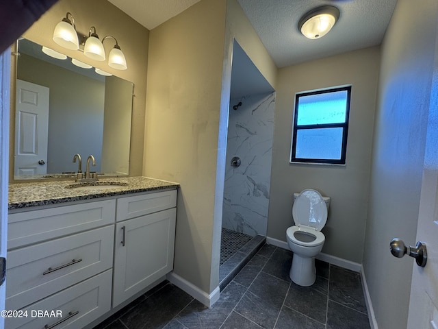 bathroom with a textured ceiling, vanity, tiled shower, tile patterned flooring, and toilet