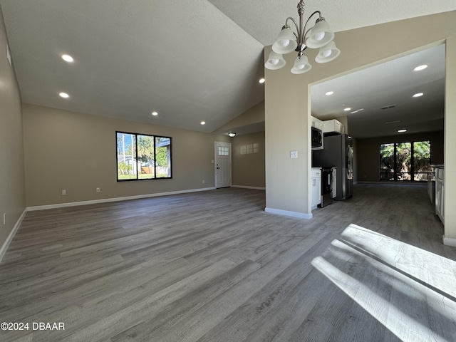 unfurnished living room with a notable chandelier, wood-type flooring, a wealth of natural light, and vaulted ceiling