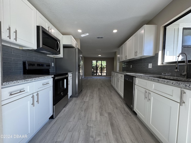 kitchen with light wood-type flooring, a textured ceiling, appliances with stainless steel finishes, light stone counters, and white cabinetry