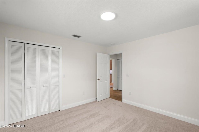 unfurnished bedroom with light carpet, a closet, and a textured ceiling