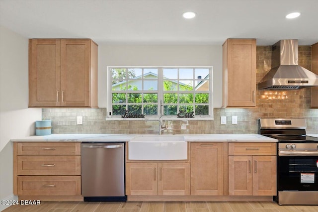 kitchen featuring a healthy amount of sunlight, stainless steel appliances, sink, and wall chimney range hood