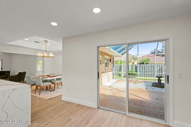 doorway with an inviting chandelier, light hardwood / wood-style flooring, and a raised ceiling