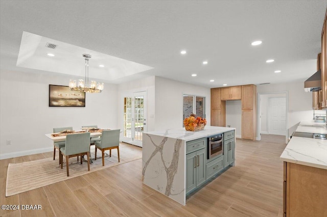 kitchen with light stone counters, hanging light fixtures, a center island, and light wood-type flooring