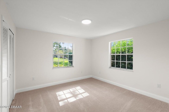 unfurnished bedroom with multiple windows, light carpet, and a closet