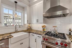 kitchen featuring tasteful backsplash, white cabinets, wall chimney exhaust hood, and stainless steel range oven