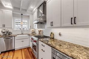 kitchen with wall chimney exhaust hood, light hardwood / wood-style flooring, beamed ceiling, white cabinets, and appliances with stainless steel finishes