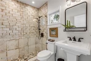 bathroom featuring a tile shower, toilet, and sink