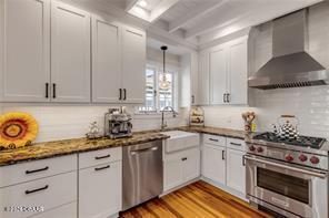 kitchen with dark stone counters, wall chimney range hood, light wood-type flooring, white cabinetry, and stainless steel appliances