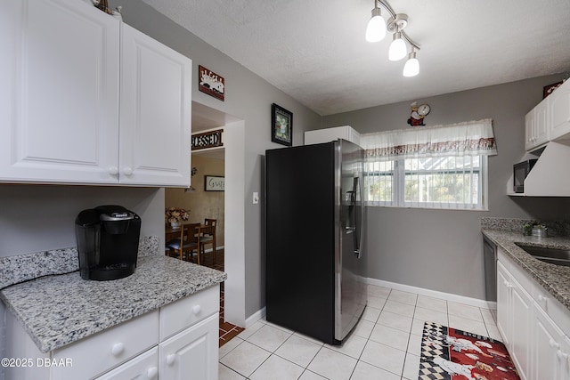 kitchen with light stone counters, a textured ceiling, light tile patterned floors, stainless steel appliances, and white cabinets