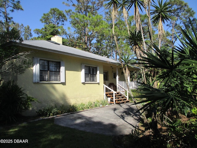 view of front facade featuring metal roof, a chimney, and stucco siding