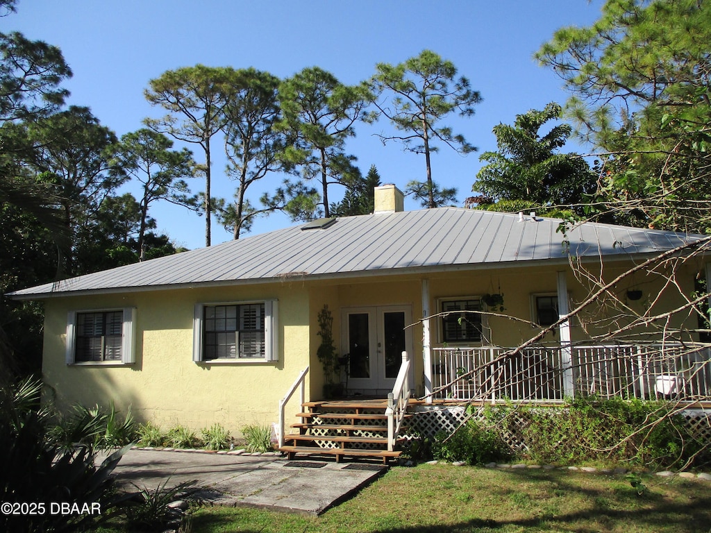 view of front of property featuring a porch, stucco siding, a chimney, french doors, and metal roof