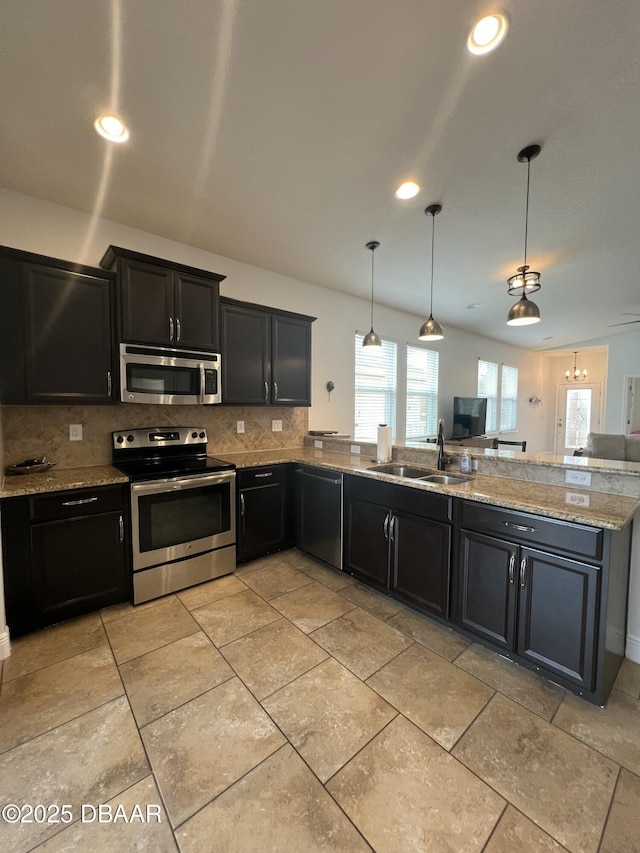 kitchen with light stone countertops, appliances with stainless steel finishes, tasteful backsplash, sink, and hanging light fixtures