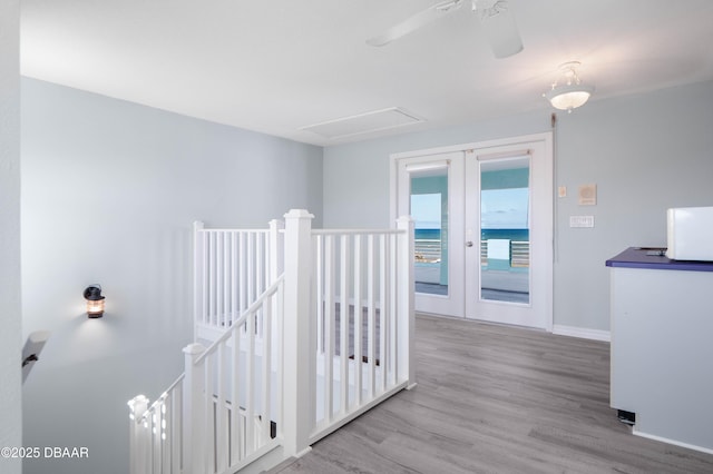 corridor with french doors, a water view, and light wood-type flooring