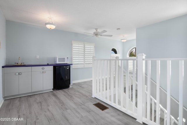 kitchen featuring sink, ceiling fan, light wood-type flooring, fridge, and white cabinetry