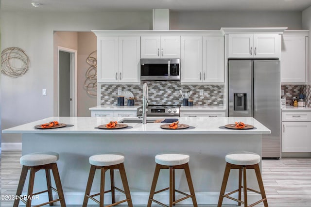 kitchen with white cabinetry, a kitchen island with sink, backsplash, and stainless steel appliances