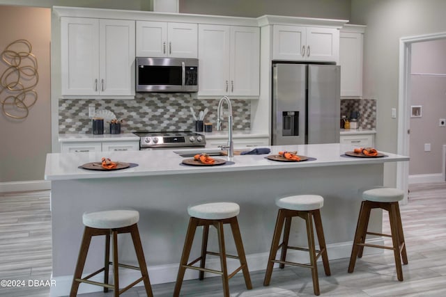 kitchen featuring white cabinetry, appliances with stainless steel finishes, tasteful backsplash, and an island with sink